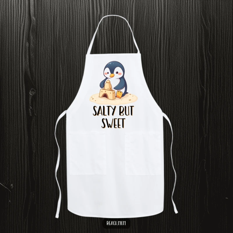 Funny penguin attempting to build a sandcastle with small flippers, printed on a kitchen apron, perfect for a humorous cooking experience.